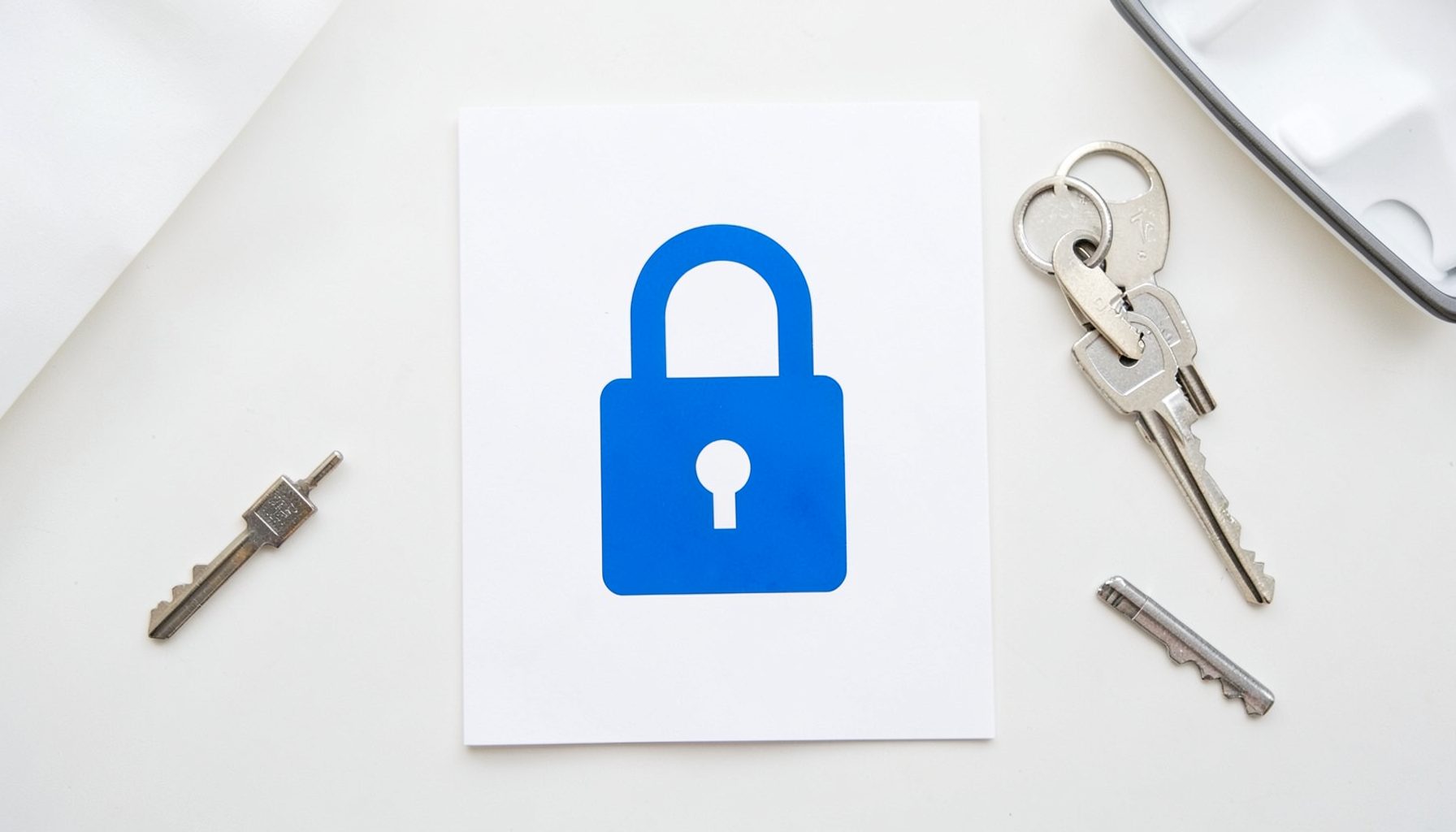 Flat-lay overhead photograph of a padlock icon on a sheet of paper, with keys on a white desk, security and trust mood